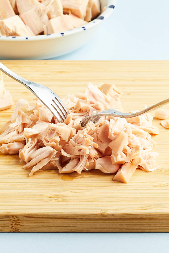 jackfruit on wooden cutting board with two forks shredding it