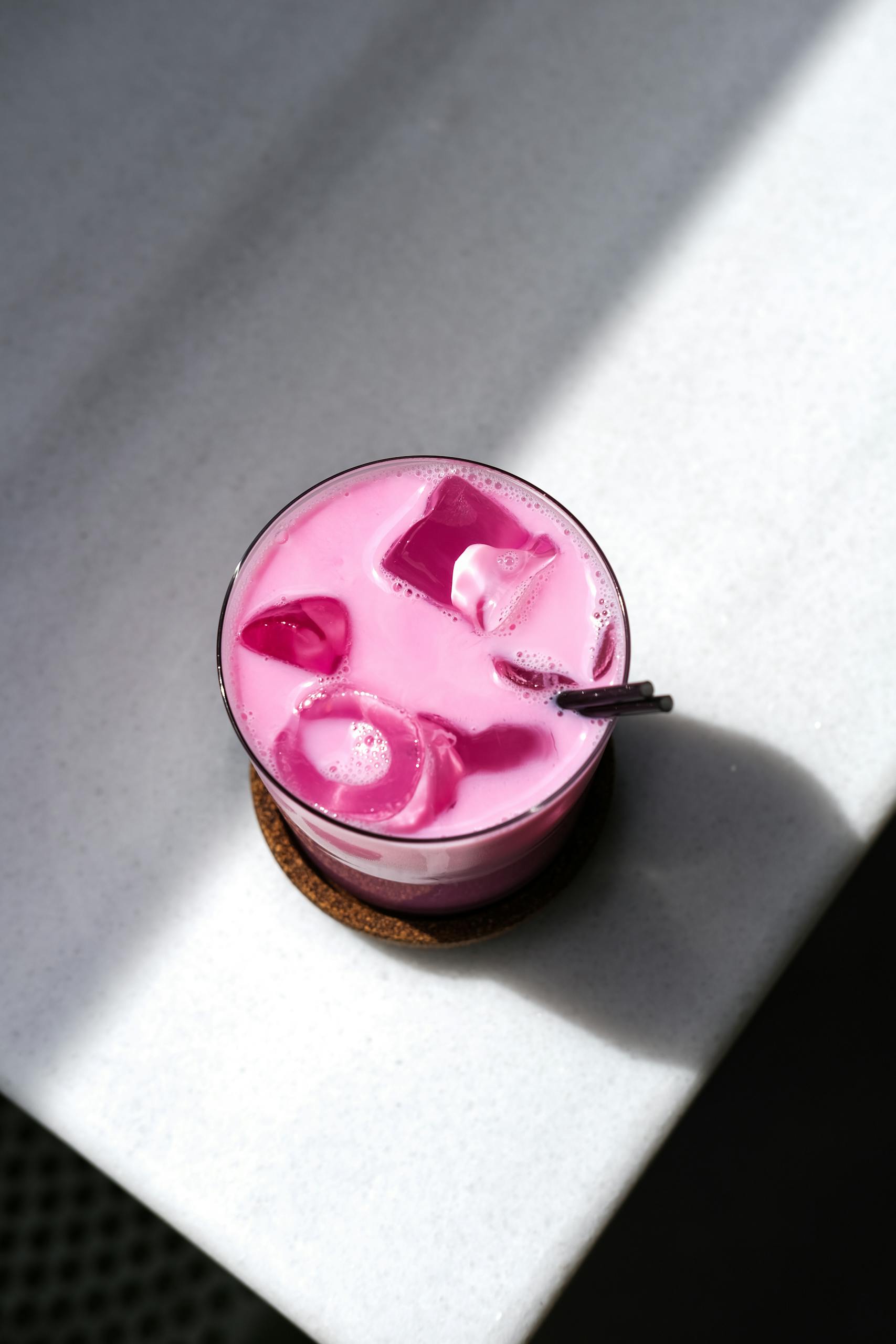 Top view of a bright pink beverage with ice cubes on a marble table.